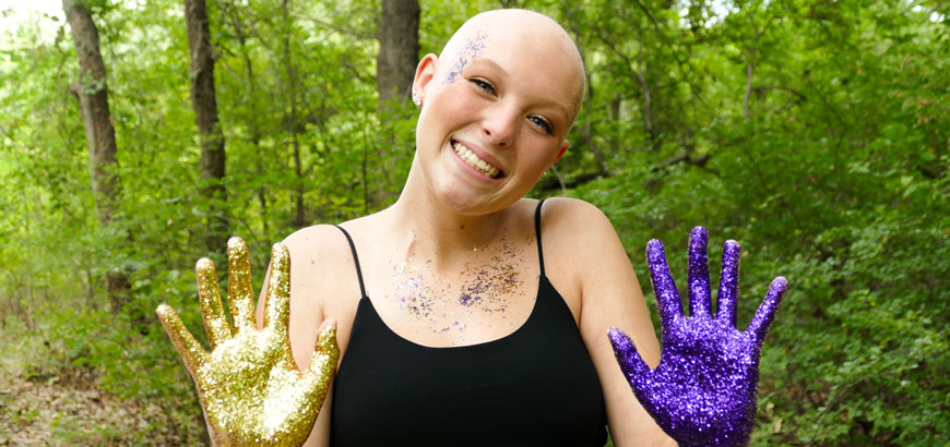 A bald woman shows her hands, one is painted purple and one painted gold.