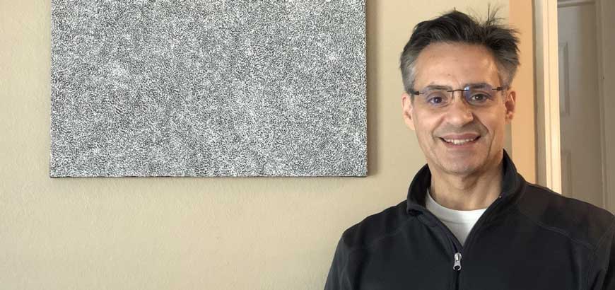 Headshot of a man standing in front a painting in his house