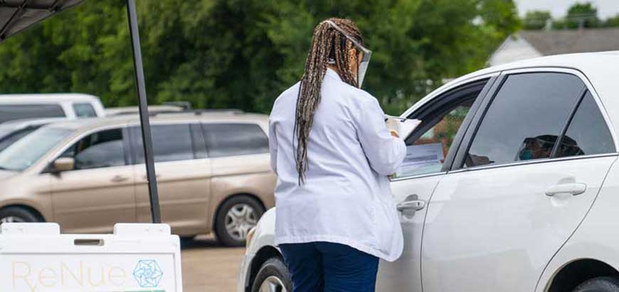 A worker speaking to a customer in their car at a drive through COVID-19 testing site