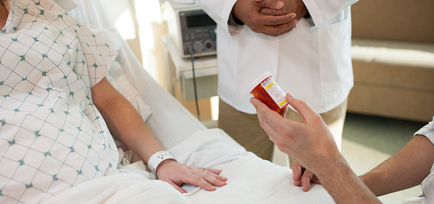 A patient lying in a hospital bed with her husband holding a prescription medication bottle