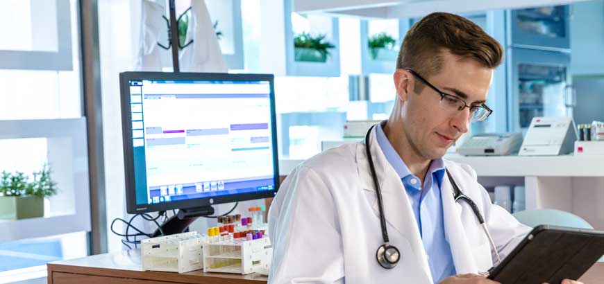 A doctor looking at a tablet standing in front of a computer workstation