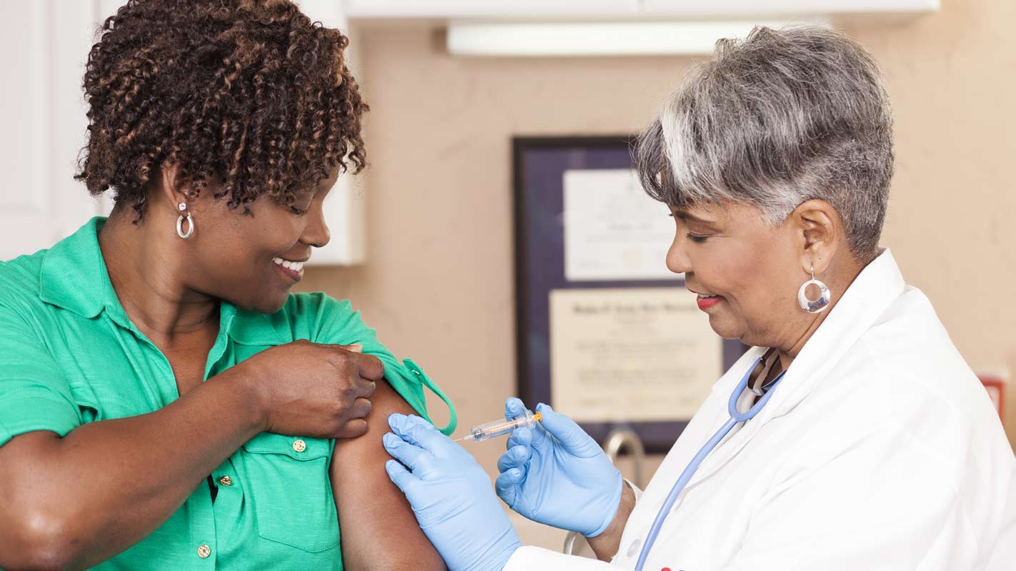 Two smiling women of color one a doctor the other a patient doctor is giving patient an injection