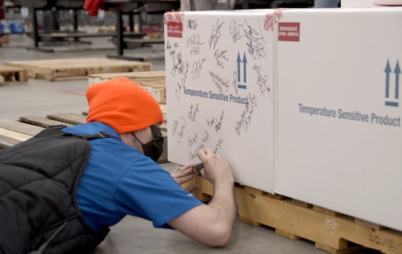 A McKesson warehouse employee signs their name to the shipping box containing the COVID vaccine