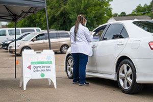 A worker talking to a person sitting in their car at a drive thru COVID-19 testing site